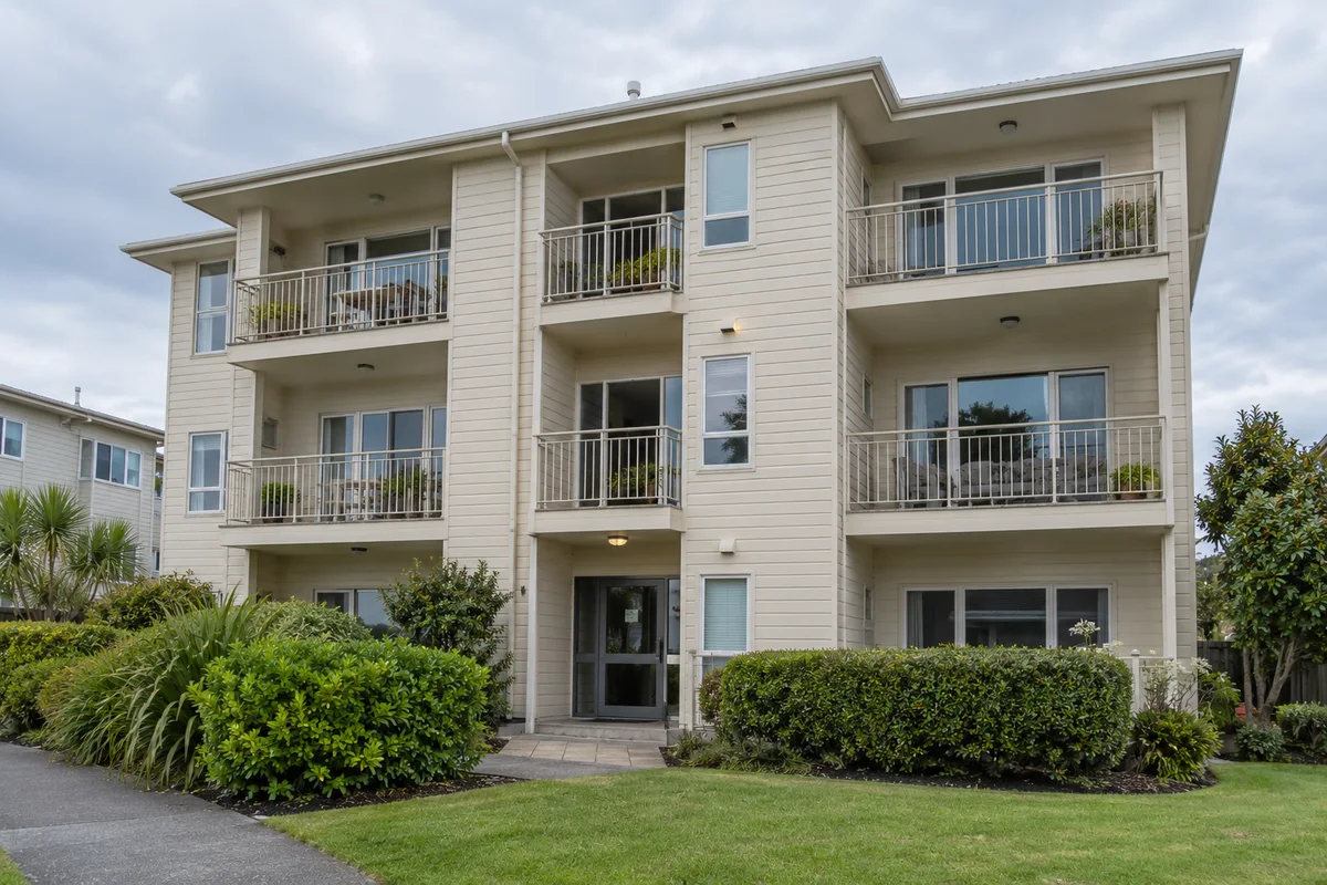A modest three-storey Auckland apartment building with painted cream cladding